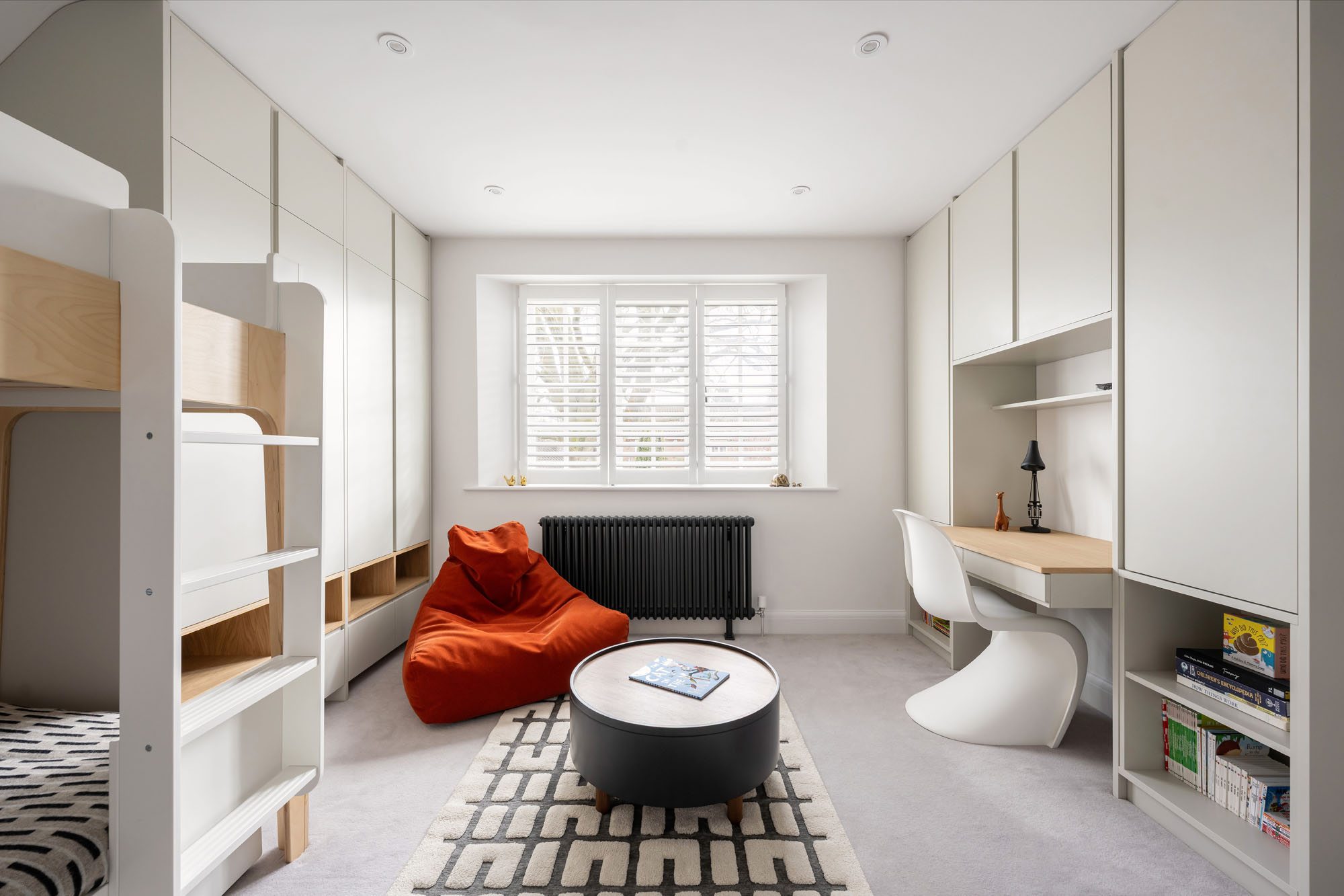 Stylish boys' bedroom by Funky Little Darlings featuring a chill-out zone with a beanbag and a storage coffee table on a graphic rug. An Oeuf NYC bunk bed and a desk with a Panton chair complete the modern, functional space.