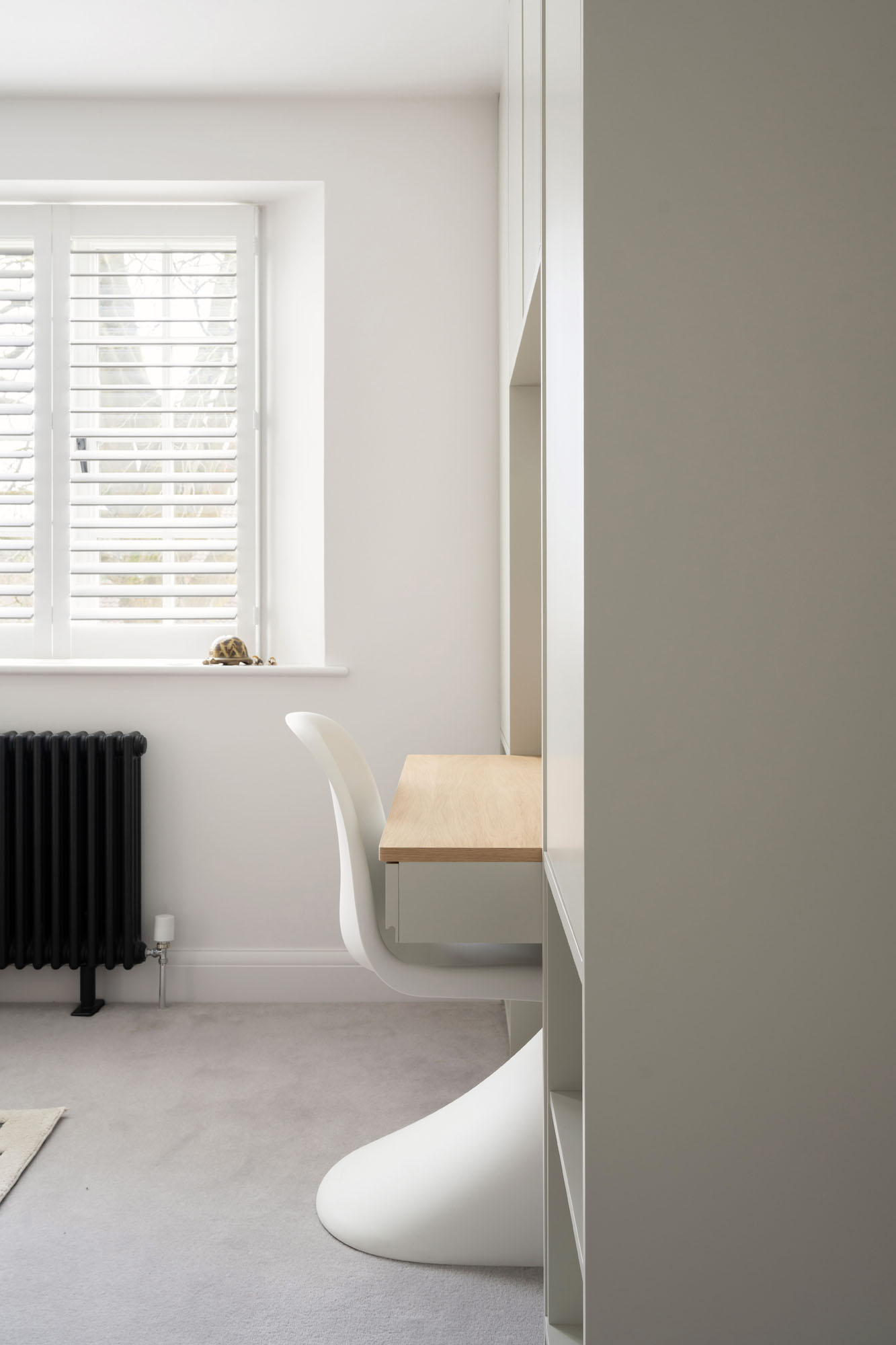 Custom-built cupboards by Funky Little Darlings with oak study desk, white Verner Panton chair, white plantation shutters, and a traditional school-style column radiator.