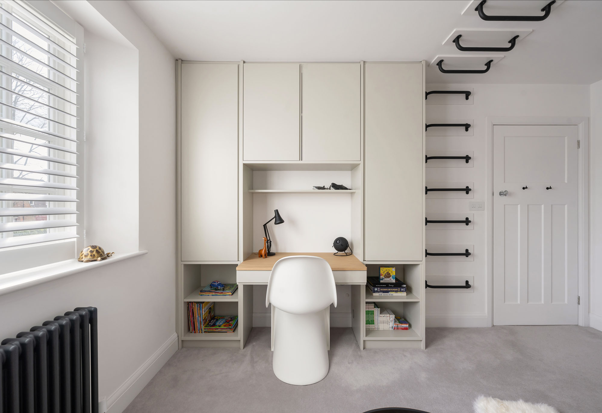 Custom-built cupboards by Funky Little Darlings with oak study desk, white Verner Panton chair, white plantation shutters, and a traditional school-style column radiator.