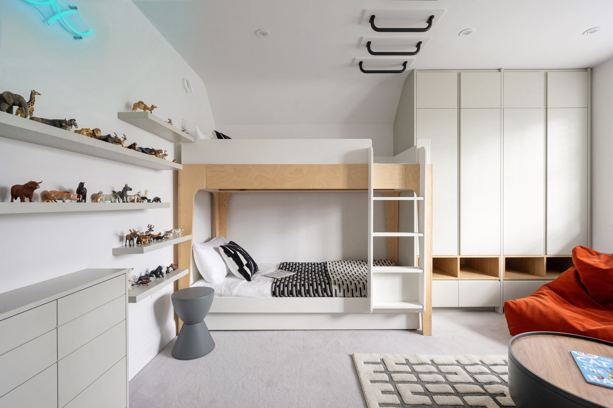 Funky Little Darlings Amersham boys’ bedroom with Oeuf NYC bunk bed, custom wardrobes, Schleich animal display shelves on wall, ceiling-mounted monkey bars, secret tunnel to sibling’s room and orange beanbag.