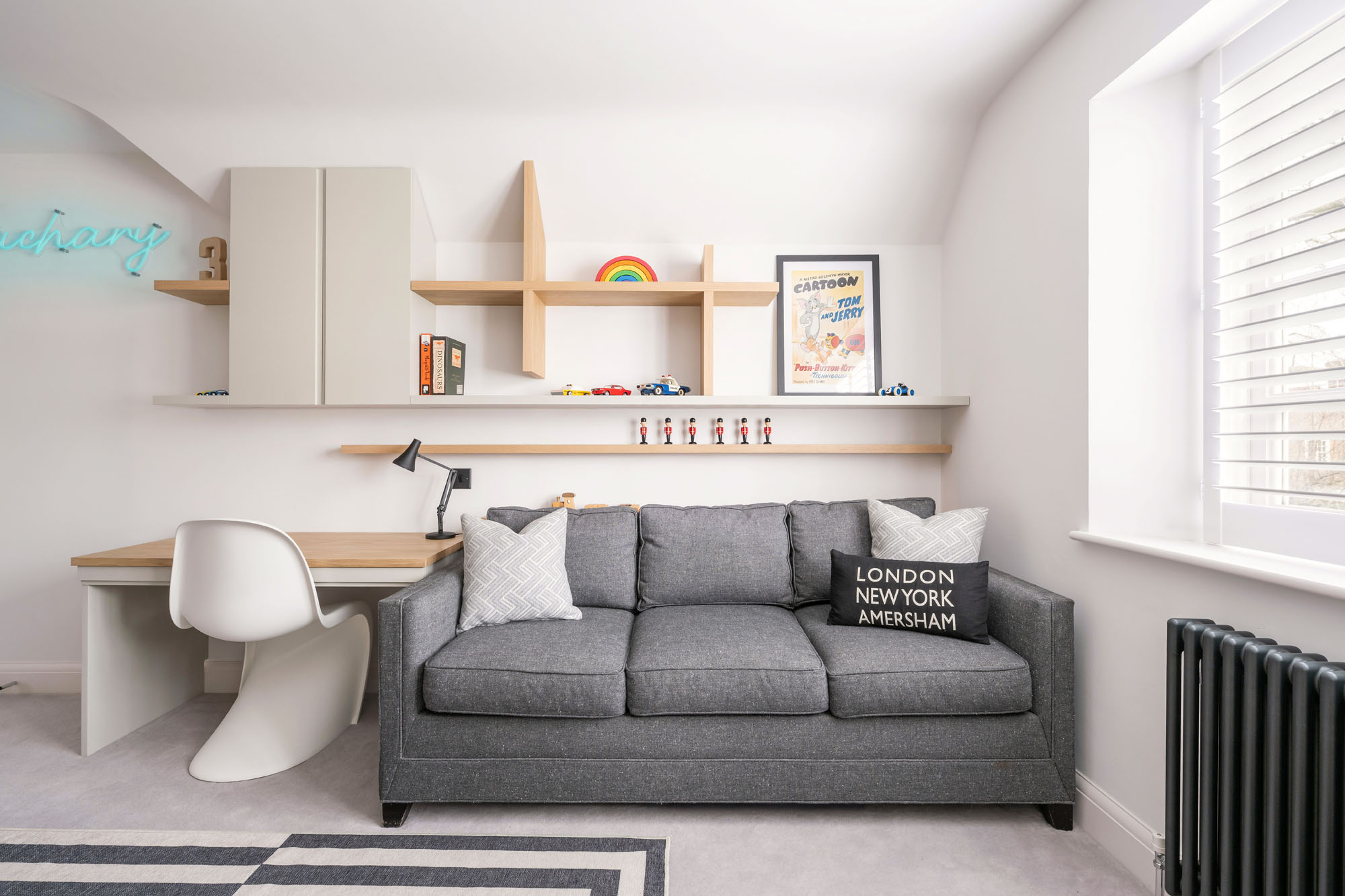Funky Little Darlings Amersham boys’ modern study area with oak desk, white Panton chair, grey sofa bed, built-in storage cupboards, oak display shelves with LED lighting, and Anglepoise desk lamp.