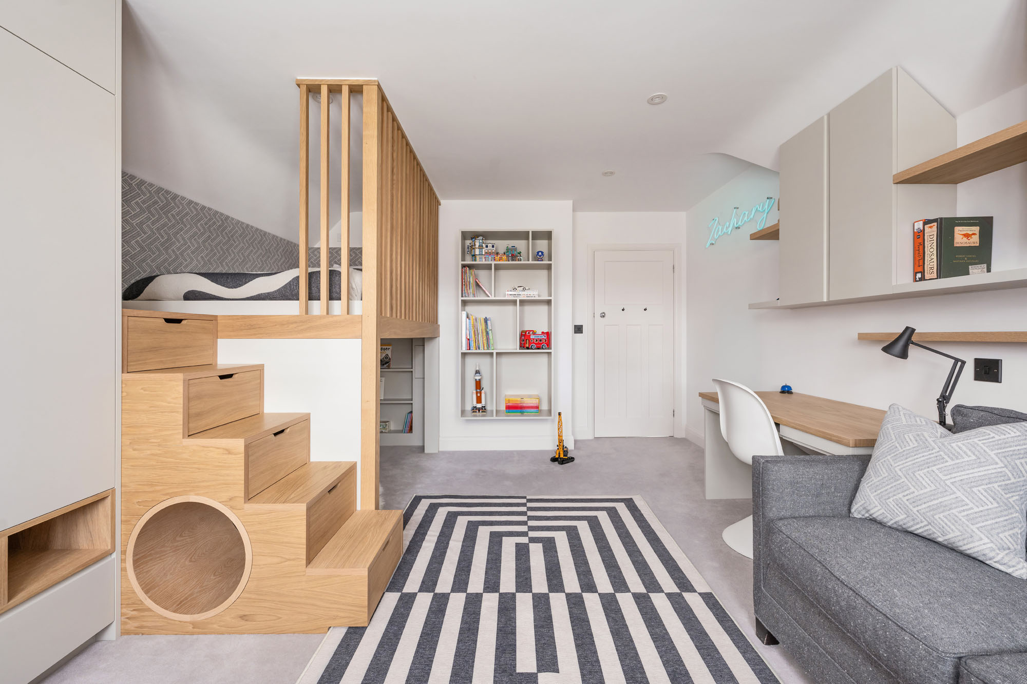 Funky Little Darlings Amersham boys bedroom with custom loft bed featuring storage steps, built-in tunnel, wall-mounted book storage, desk, and chair in this playful and functional kids room design.