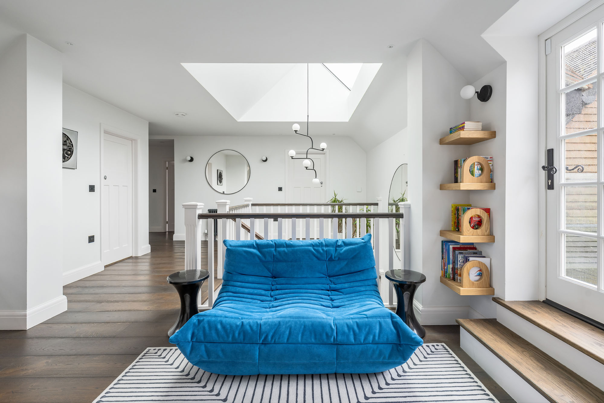 Spacious boys’ hallway in Amersham designed by Funky Little Darlings, with a blue Togo sofa by Ligne Roset, Tam Tam stools as side tables, Jonathan Adler rug and a mini library.