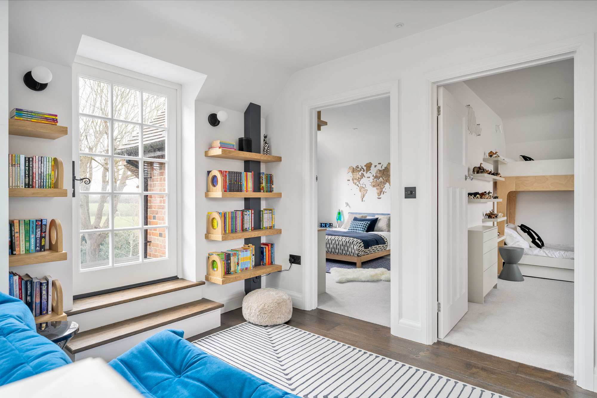 Spacious boys’ hallway in Amersham designed by Funky Little Darlings, with a blue Togo sofa by Ligne Roset, Tam Tam stools as side tables, Jonathan Adler rug and a mini library.