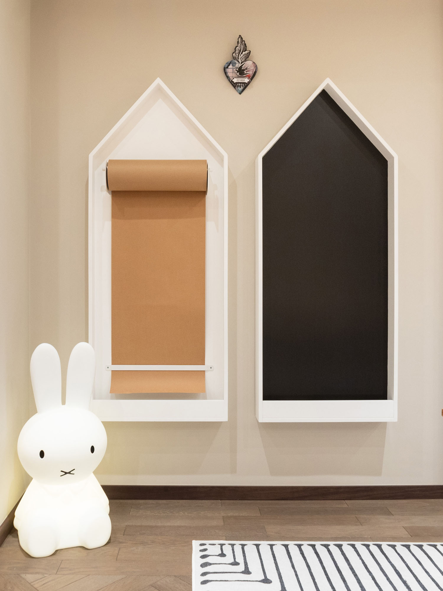 Creative art corner in children’s playroom in Cobham designed by Funky Little Darlings, featuring a Miffy floor lamp, wall-mounted house-shaped paper roll holder and chalkboards with a modern craft table. A thoughtfully designed space blending creative play with contemporary kids’ interior design elements.