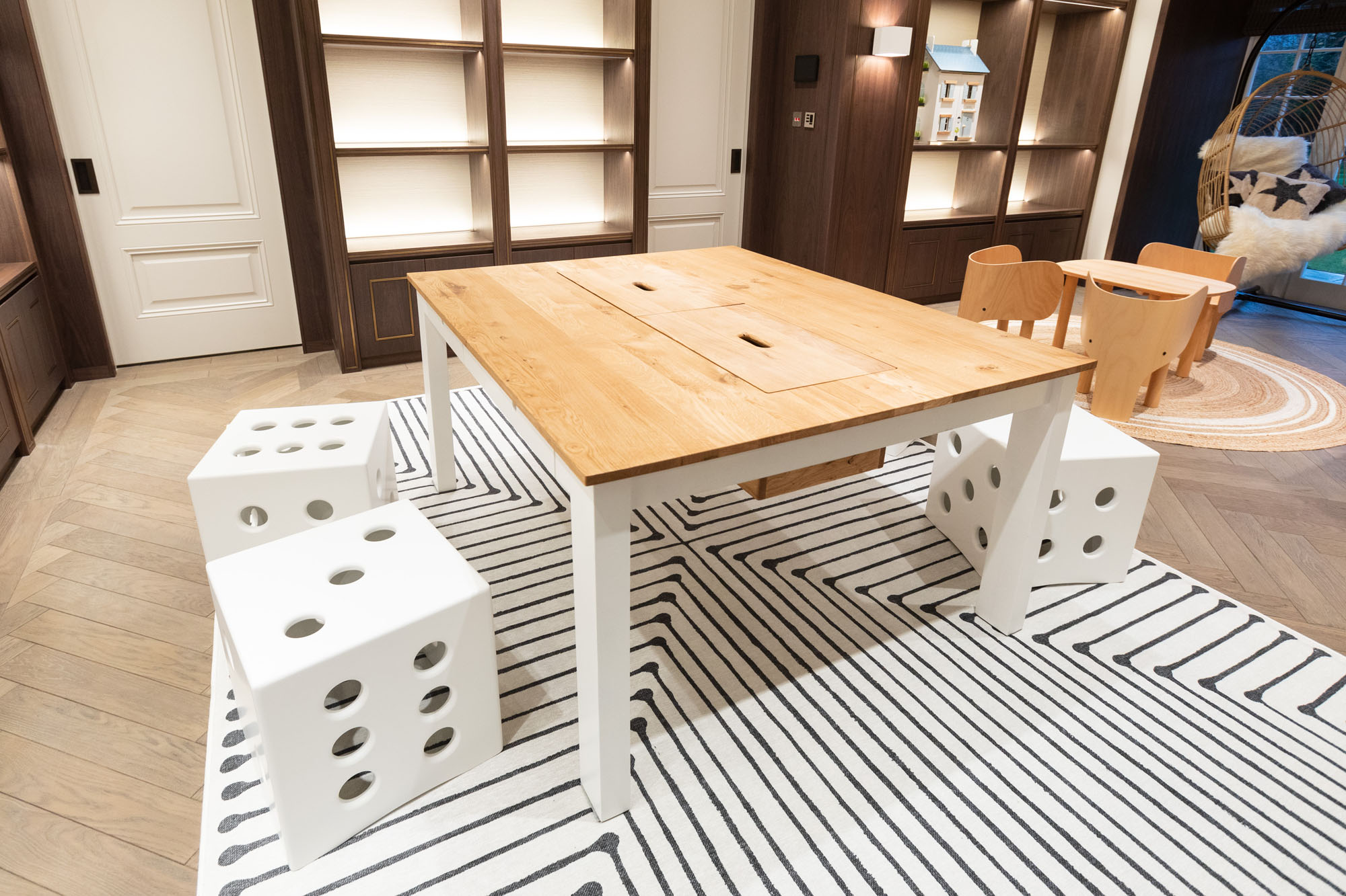This Funky Little Darlings Cobham playroom features an oak-topped craft table paired with white dice-shaped stools, set on a Jonathan Adler washable rug. The space is completed with EO Elephant chairs and modern display shelves designed to make children’s playtime fun and organised.