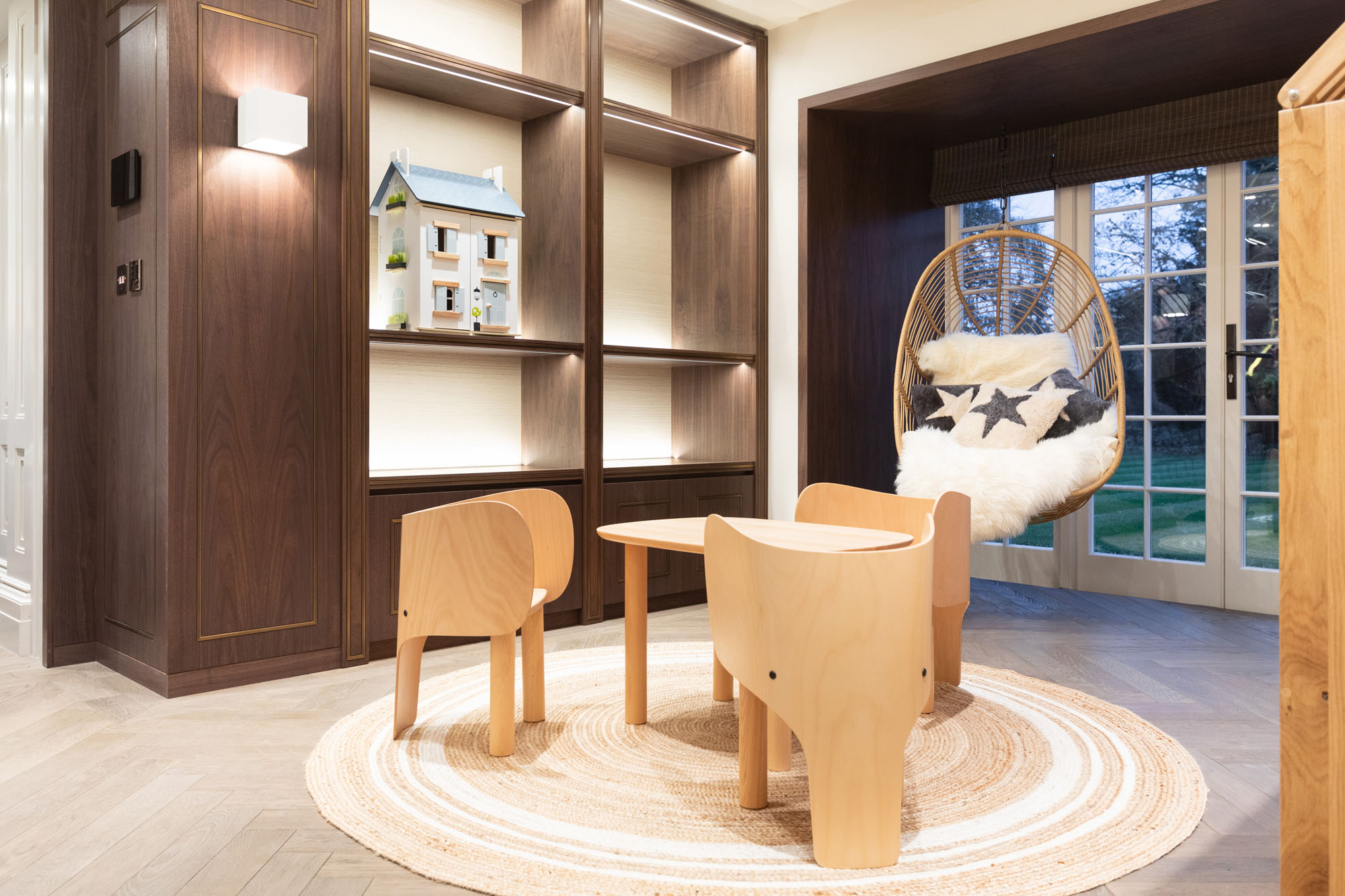 Contemporary children’s playroom in Cobham designed by Funky Little Darlings, featuring a playful play table with elephant chairs, a cosy hanging swing chair piled with cushions and stylish open display shelves. A fun and functional space blending imaginative design with funky kids’ room decor.