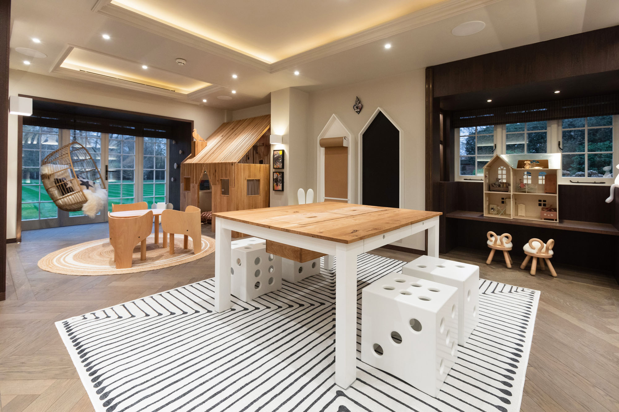 Beautifully designed and multi-zoned children’s playroom in Cobham by Funky Little Darlings, featuring a charming indoor playhouse, play table with EO elephant chairs, craft table with oversized white dice stools, drawing corner, a cosy hanging swing chair, a whimsical Maileg dolls house and iconic EO sheep stools. A playful, luxurious multi-functional space blending imaginative design with functional, modern kids’ interiors.