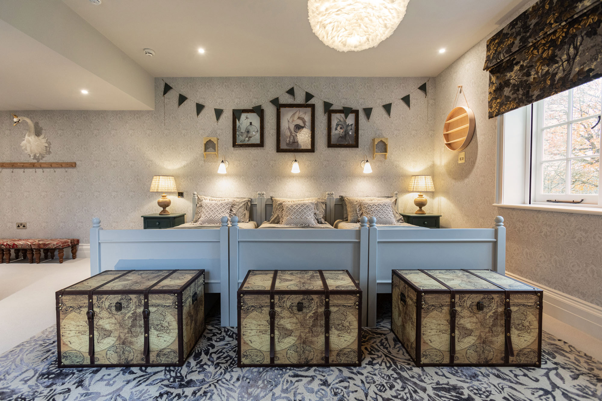 Shared triple children’s bedroom in Cobham designed by Funky Little Darlings, featuring three single beds with vintage storage trunks, traditional William Morris wallpaper and patterned rug that enhances the room’s nostalgic, heritage-inspired charm.