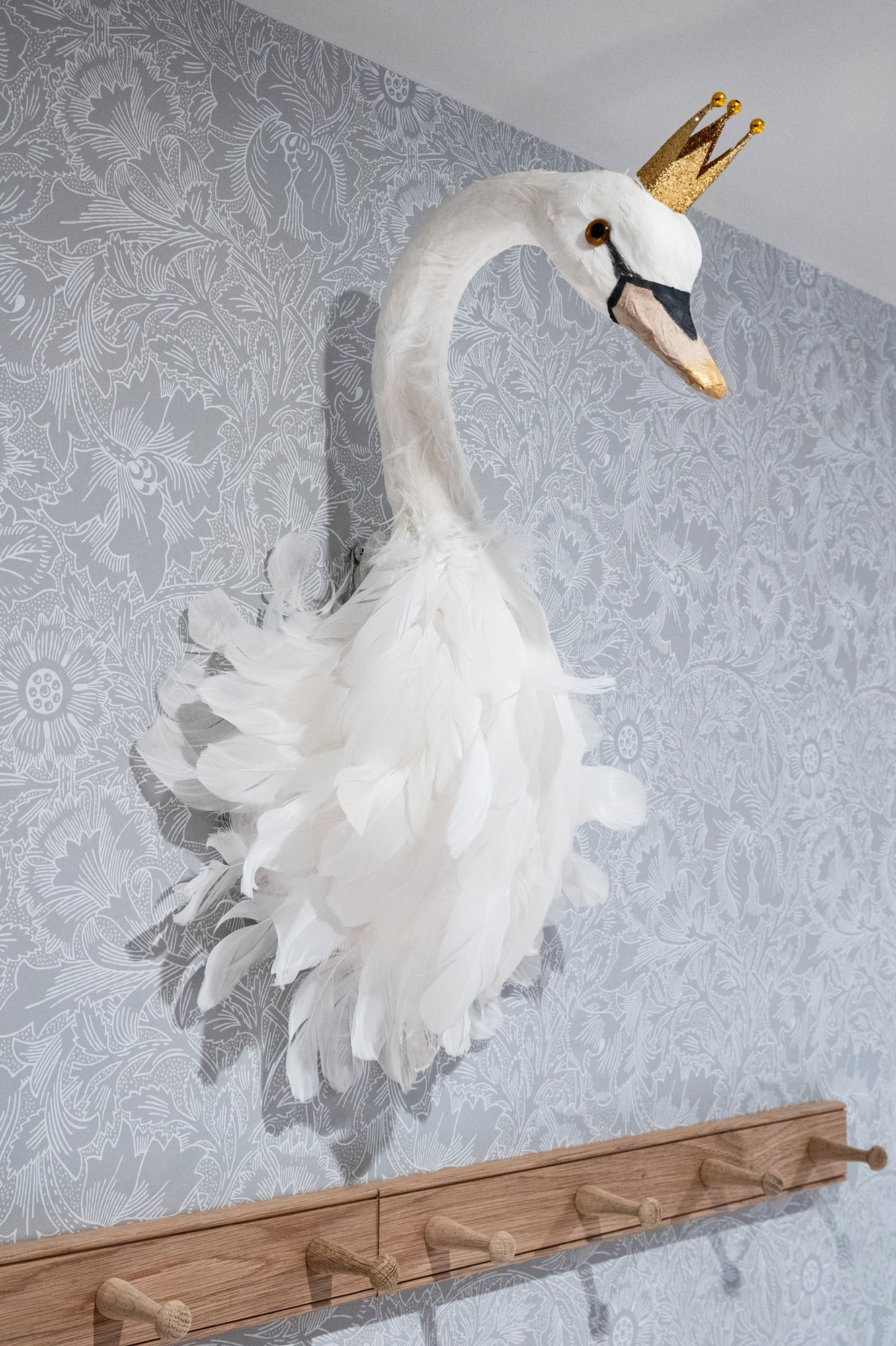 Charming shared triple bedroom in Cobham designed by Funky Little Darlings, featuring whimsical swan head wall decoration, Shaker oak coat hooks and elegant William Morris Pure Poppy wallpaper blends imaginative details with timeless British interior design for children.