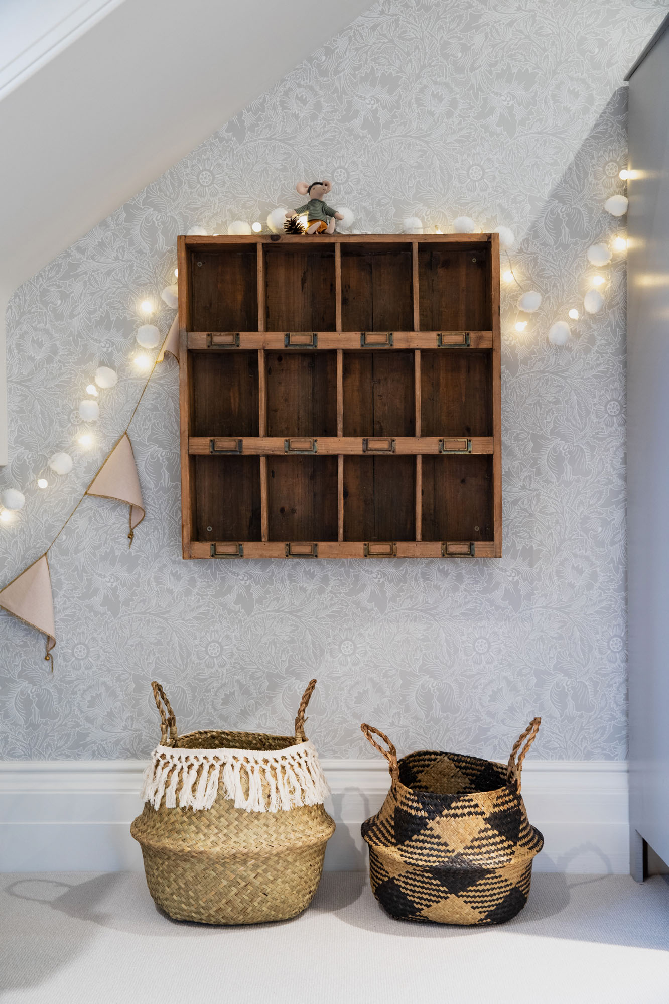 Shared triple children's bedroom in Cobham by Funky Little Darlings, featuring vintage wooden shelf, woven belly baskets, warm fairy lights and classic William Morris botanical wallpaper creates a playful, boho-chic interior design for kids.