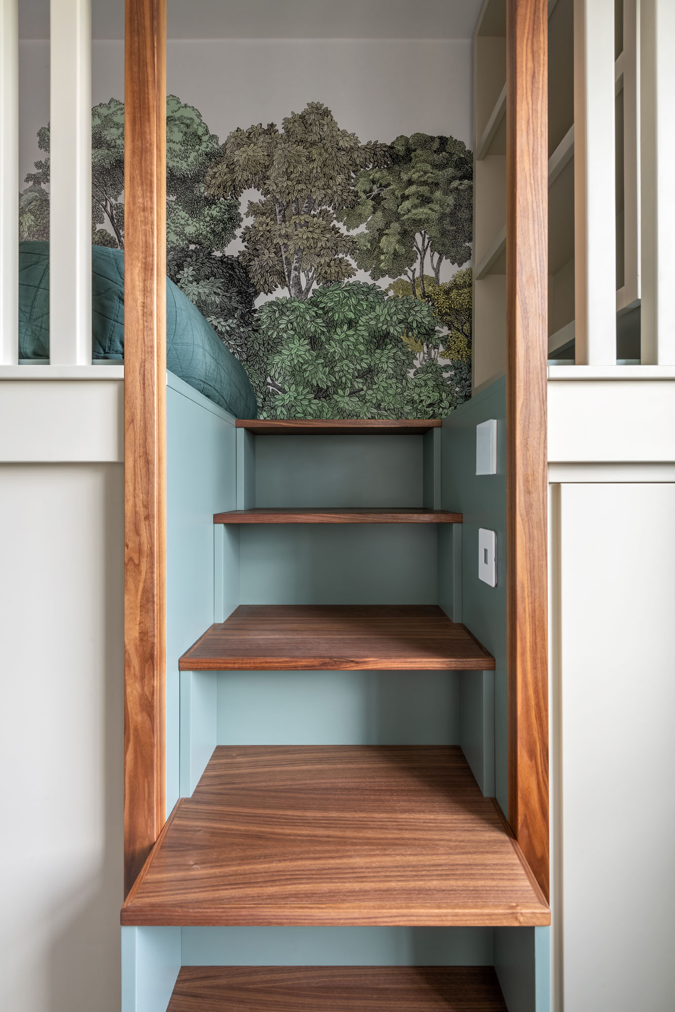 Stylish Hampstead boy’s bedroom designed by Funky Little Darlings, featuring a raised cabin bed with integrated storage steps painted in Little Greene Livid with walnut detailing, set against a lush Rebel Walls Bellewood forest mural for a cosy, nature-inspired look.