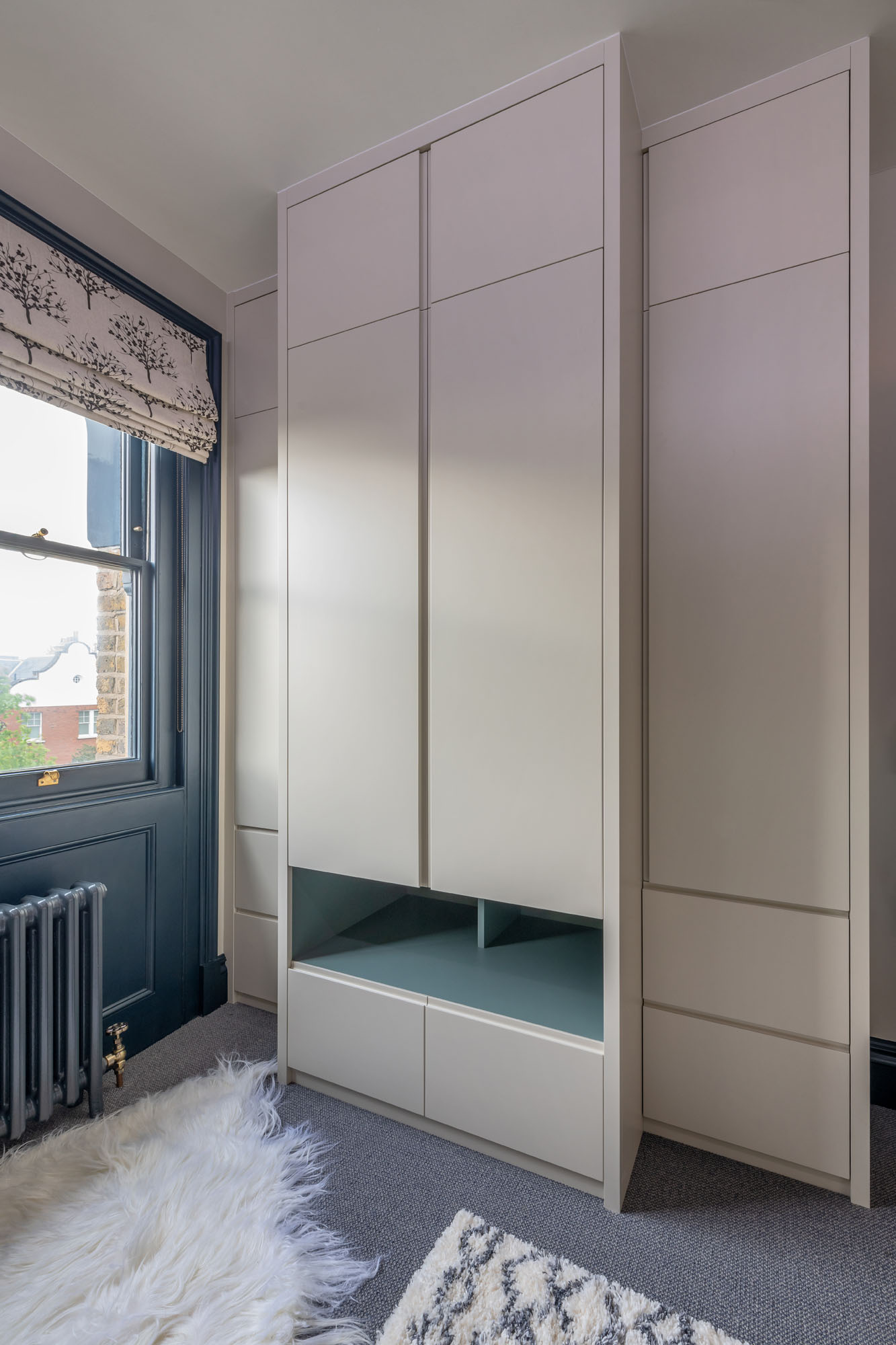 Functional wardrobe storage in a stylish boy's bedroom by Funky Little Darlings in Hampstead, featuring a modern stepped-back triple wardrobe with drawers and open display cubby holes for organised and accessible storage solutions.