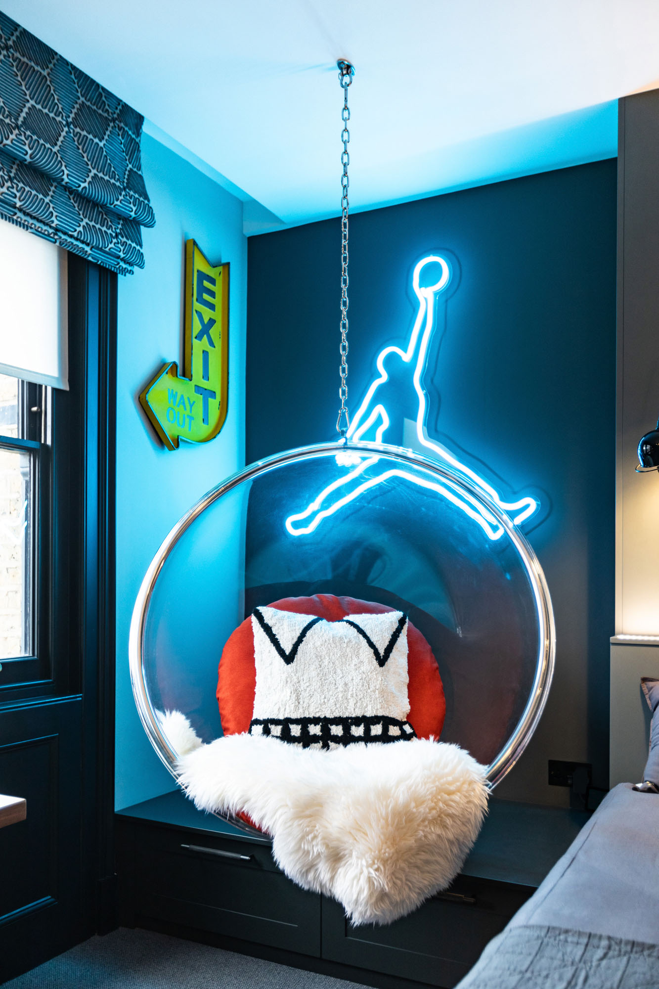 A contemporary boy’s bedroom in Hampstead by Funky Little Darlings, showcasing a vibrant turquoise Michael Jordan neon sign and a clear hanging bubble chair. This stylish children’s room interior blends playful, modern accents with elegant built-in storage for a perfect balance of fun and functionality.