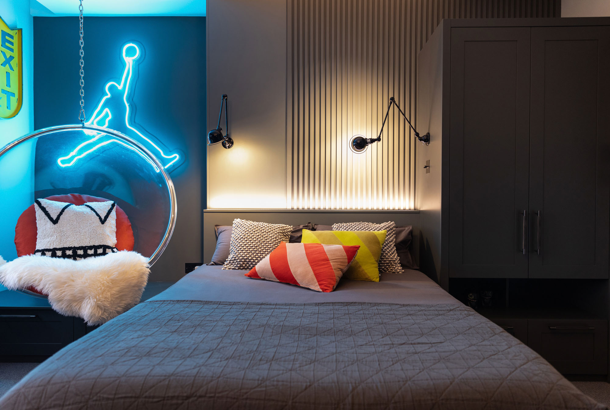 Stylish Hampstead boy’s bedroom by Funky Little Darlings featuring a bespoke bed with slatted wood wall panelling, vibrant neon sign, clear hanging bubble chair, and industrial Jielde Signal wall lights creating a modern, design-led kids' space with personality and flair.