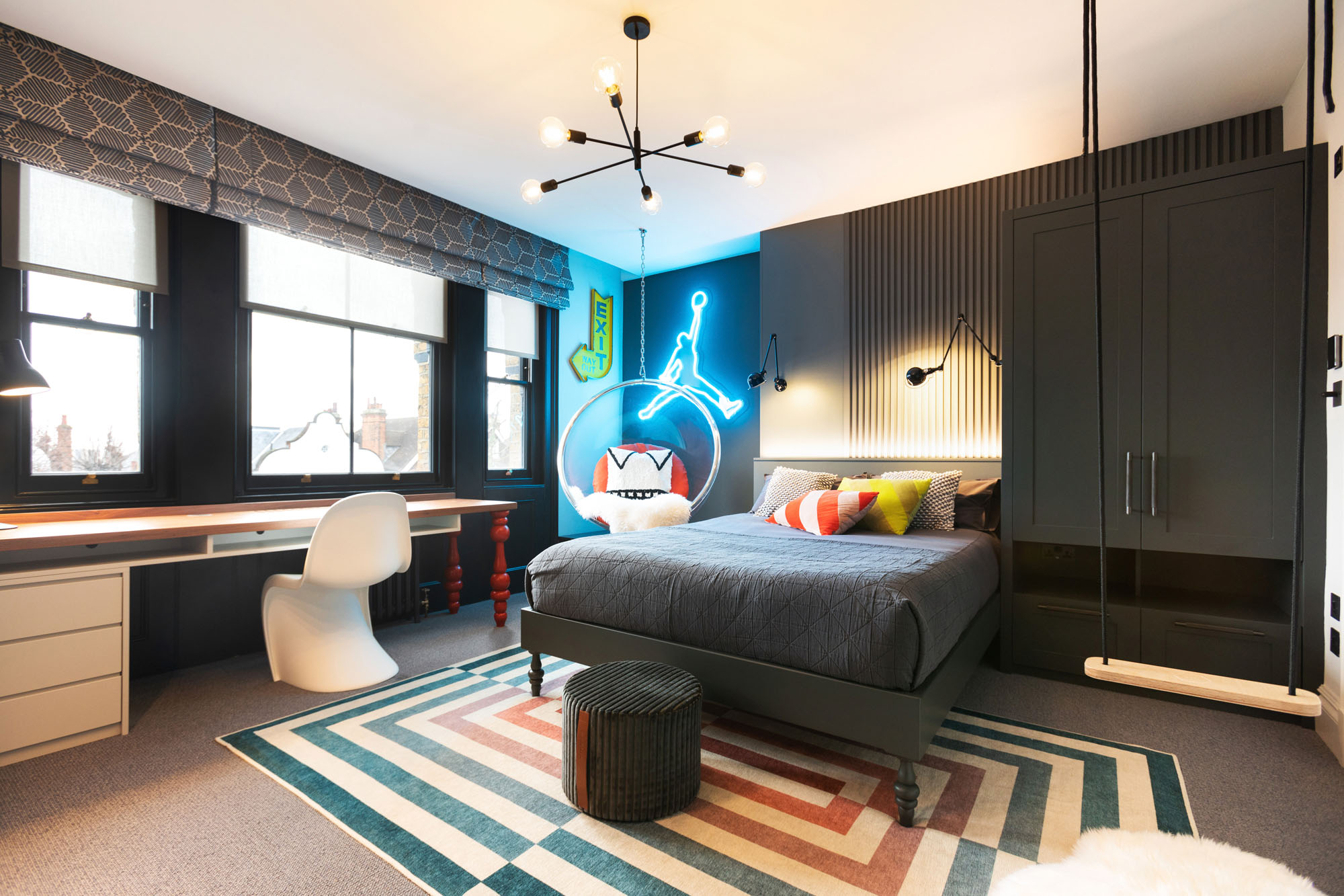 Vibrant Hampstead boy's bedroom featuring a custom designed bed and built-in wardrobes, playful indoor swing and a Michael Jordan neon sign. Includes a clear hanging bubble chair, bold Jonathan Adler rug, modern desk with white Panton chair, and colourful Missoni pouffe, designed by Funky Little Darlings.