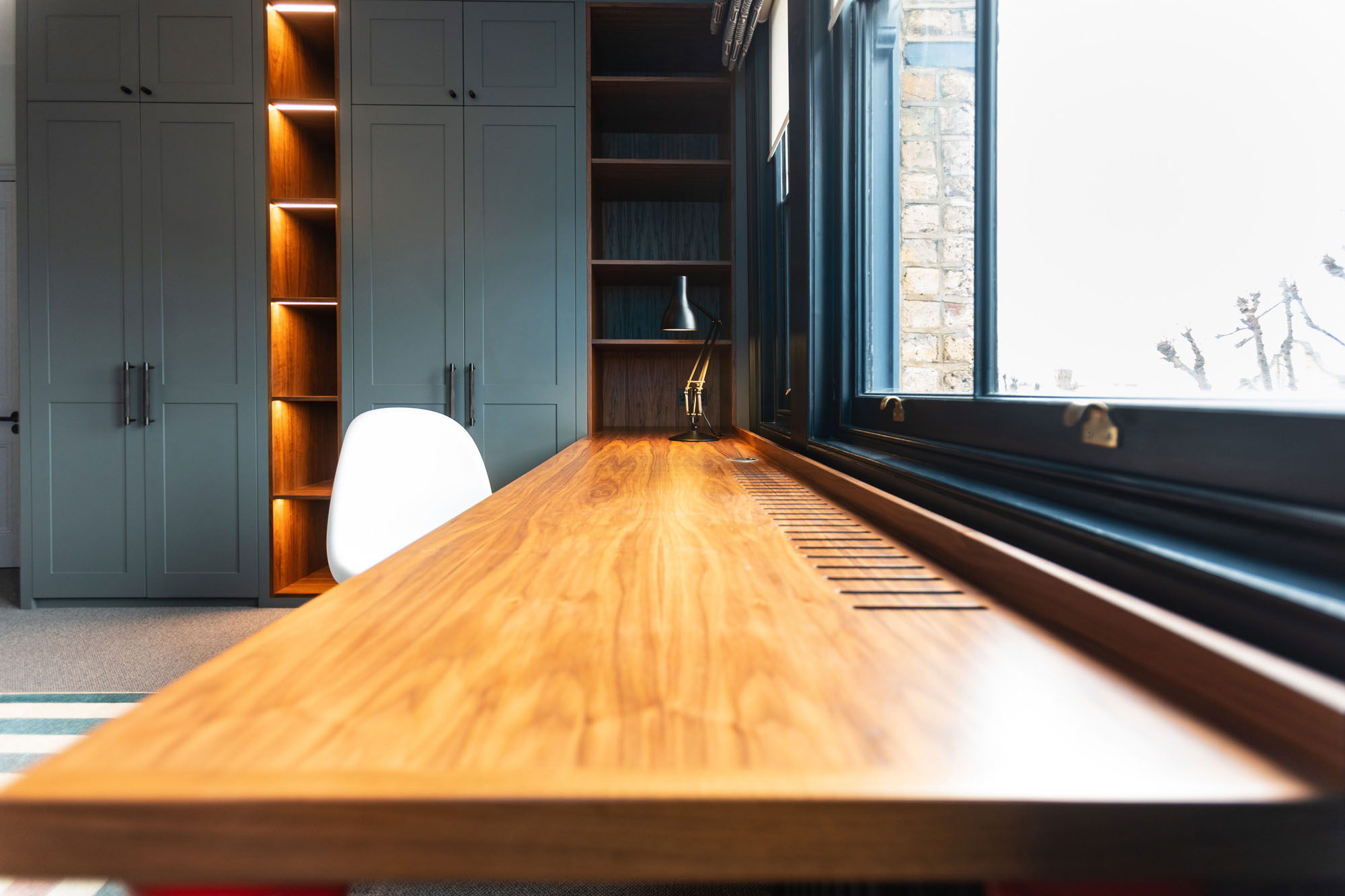 Contemporary Hampstead boy’s bedroom designed by Funky Little Darlings featuring a long bespoke walnut desk cleverly integrated into cupboard space, custom built-in wardrobes providing storage and LED illuminated display shelves, and smart, space-saving design solutions combining functionality and modern style.