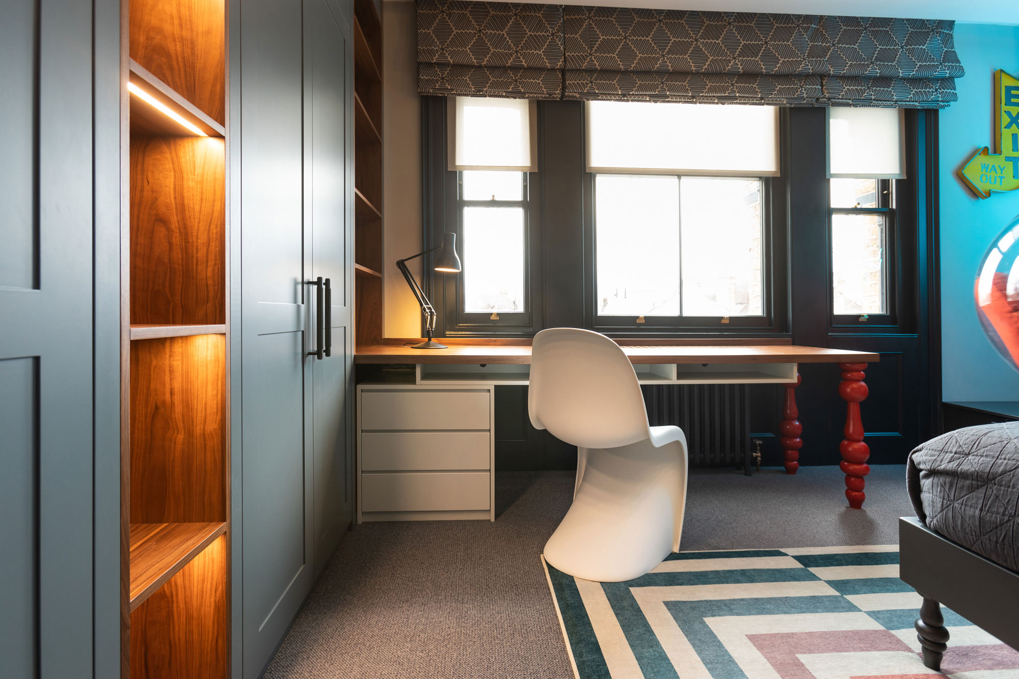 Colourful, modern Hampstead boy’s bedroom designed by Funky Little Darlings featuring bespoke walnut desk with pedestal storage and red turned legs, white Verner Panton chair, Jonathan Adler rug and built-in wardrobe storage, blending stylish furniture and practical organisation in a modern children’s room.