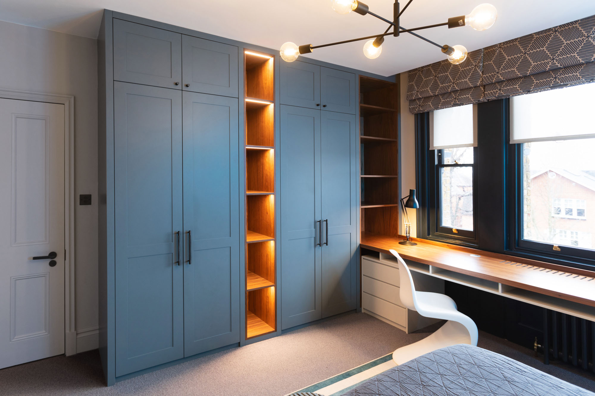 Contemporary Hampstead boy’s bedroom designed by Funky Little Darlings featuring bespoke desk with pedestal storage, sleek white Panton chair, built-in wardrobes with open display storage shelves illuminated with LED lighting and industrial multi-arm pendant ceiling light, combining modern design with practical organisation in a stylish children’s room.